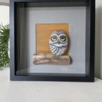 Handgemaakt kunstwerk van beschilderde uil op grote pebblestone zittend op drijfhout.
