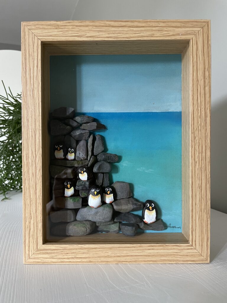 Ingelijst kunstwerk met handbeschilderde pebblestones als pinguïns op rotsen en zee van acrylverf