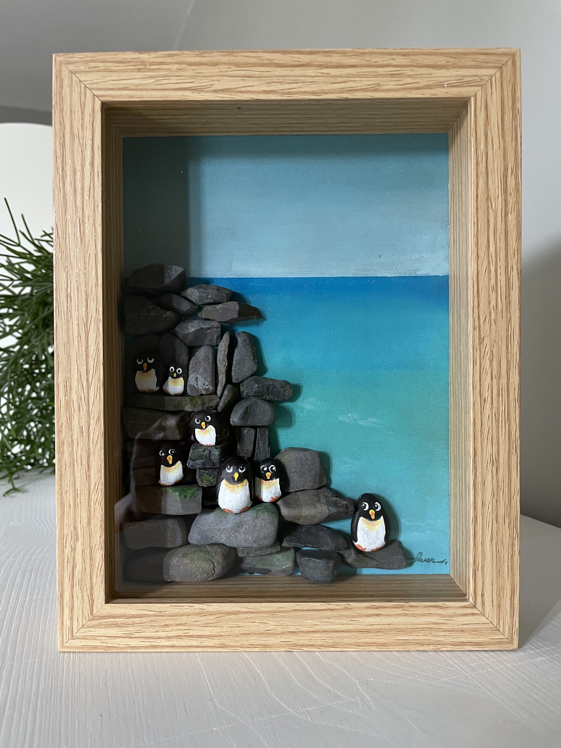 Ingelijst kunstwerk met handbeschilderde pebblestones als pinguïns op rotsen en zee van acrylverf