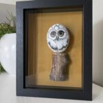 Handbeschilderde uil op grote pebblestone zittend op een stuk drijfhout, ingelijst kunstwerk.