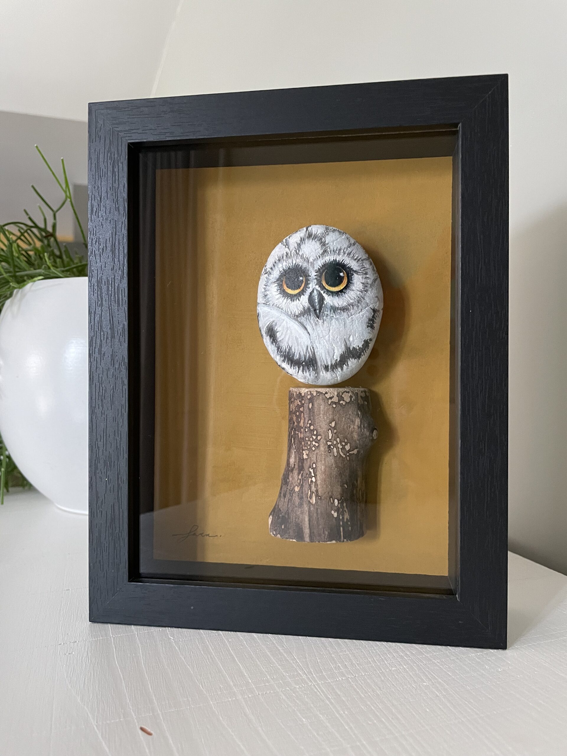 Handbeschilderde uil op grote pebblestone zittend op een stuk drijfhout, ingelijst kunstwerk.
