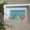 Kunstwerk met flamingo’s van handbeschilderde keitjes in een serene baai, omlijst in een dieptelijst.
