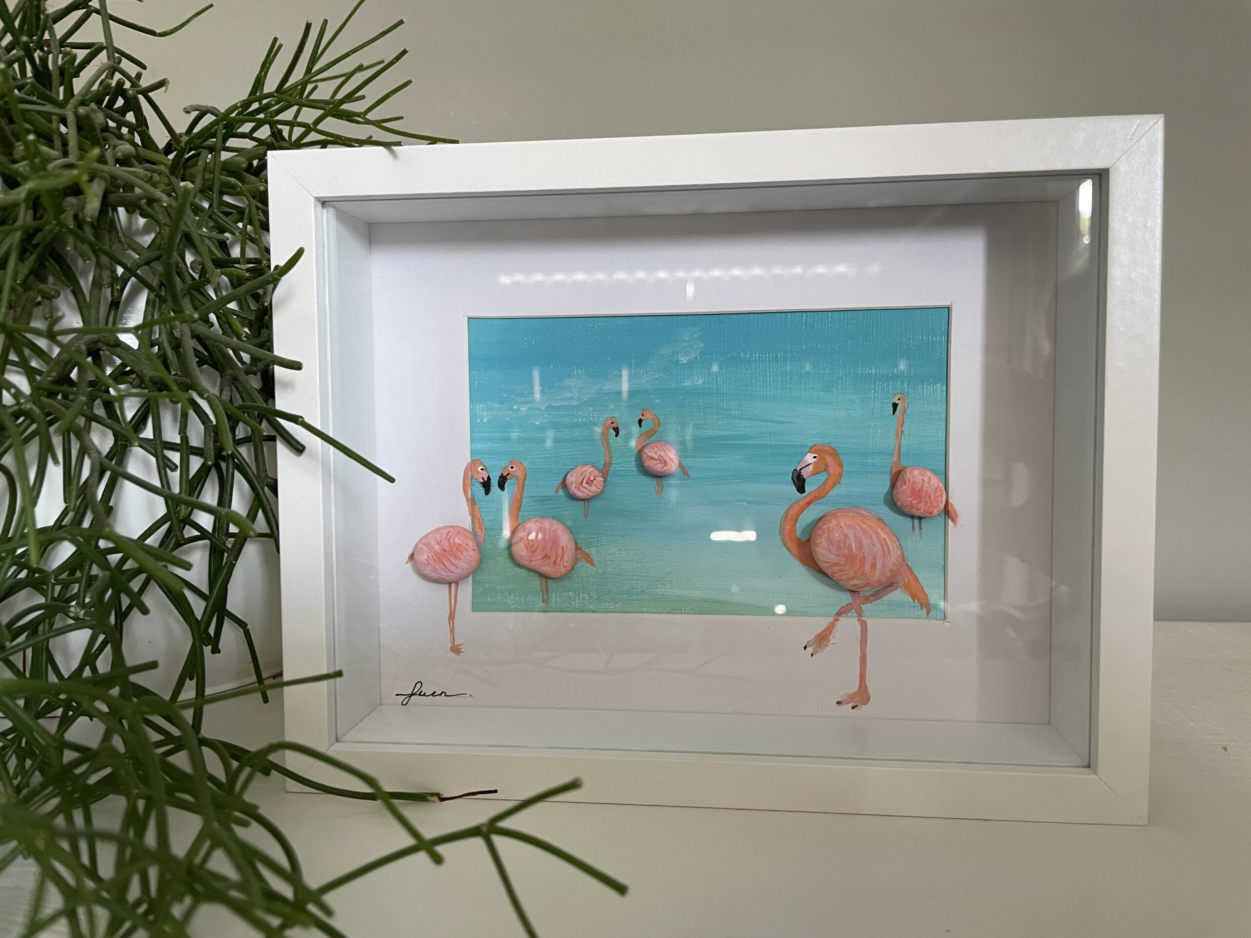 Kunstwerk met flamingo’s van handbeschilderde keitjes in een serene baai, omlijst in een dieptelijst.