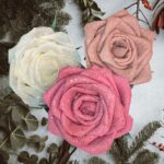 Drie handgemaakte papieren rozen in crème, blush en roze tinten met glitters, sfeervol gepresenteerd tussen wintergroen en kerstgroen, perfect als elegante kerstdecoratie